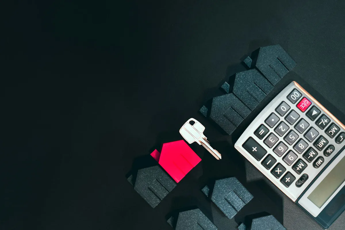 House key, small model home and a calculator laid out on a dark desk