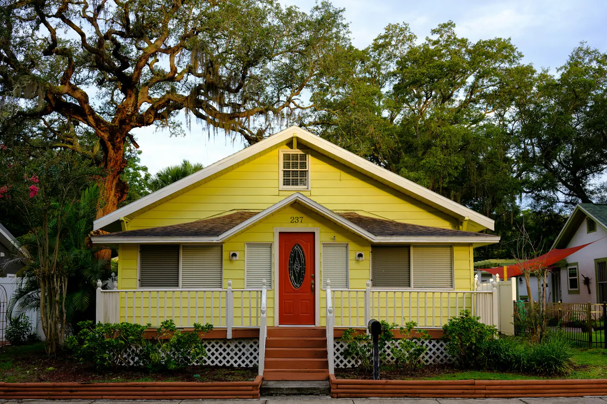 Yellow Florida bungalow with a front porch under a live oak tree