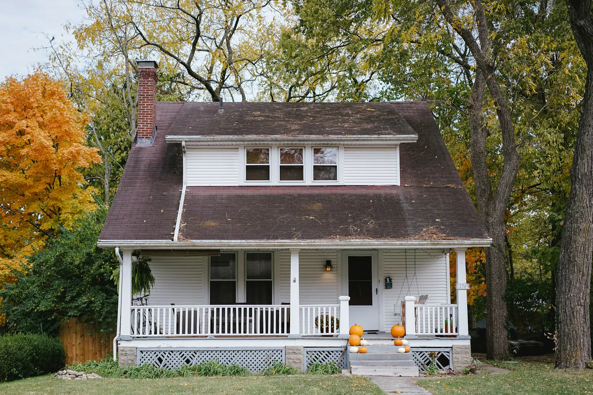 White Ohio farmhouse with a wraparound porch in autumn
